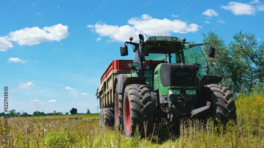 Rape Seed Harvesting. A big agricultural tractor with a yellow in a huge endless sunny field in a rural area. Transportation of oilseed rape crop after being harvested by combine harvester during Rape Seed Harvesting. A big agricultural tractor with a yellow in a huge endless sunny field in a rural area. Transportation of oilseed rape crop after being harvested by combine harvester during