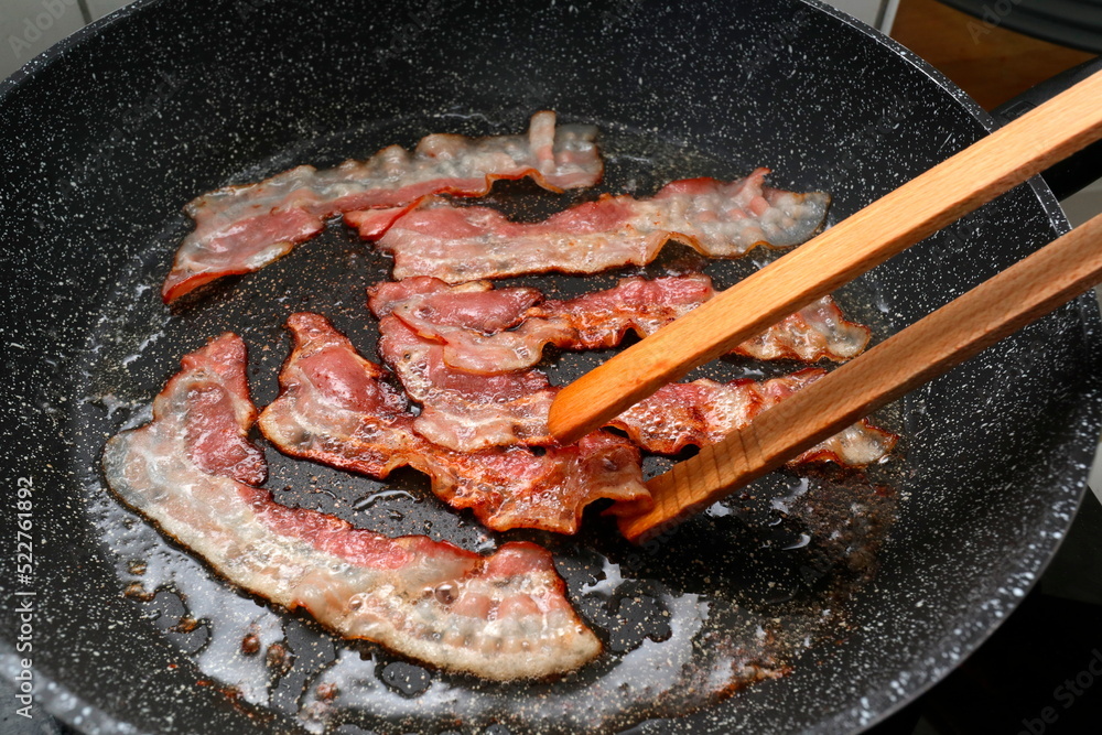 gebratener Speck in Bratpfanne mit Holzzange