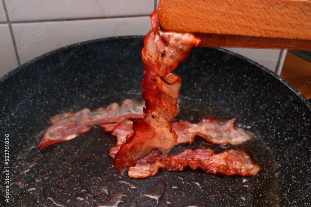 gebratener Speck in Bratpfanne mit Holzzange