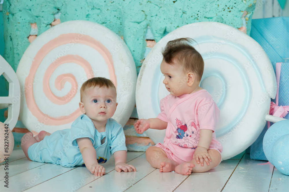A two baby lies on a soft surface in a bright room, dressed in blue and pink clothing. The concept of childhood and baby care.
