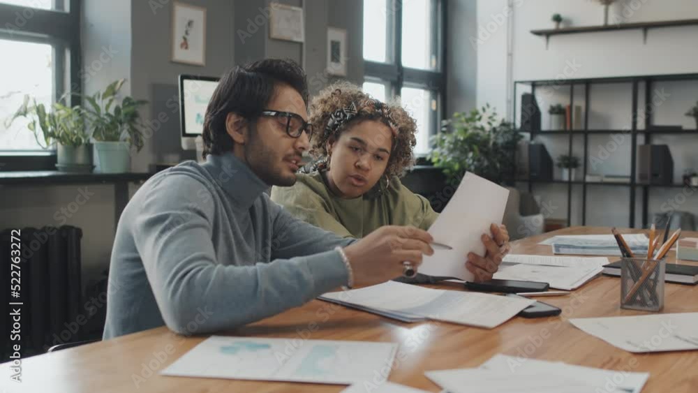 Medium of African American girl and young Middle Eastern man sitting at table in conference room, having conversation, working with documents Medium of African American girl and young Middle Eastern man sitting at table in conference room, having conversation, working with documents