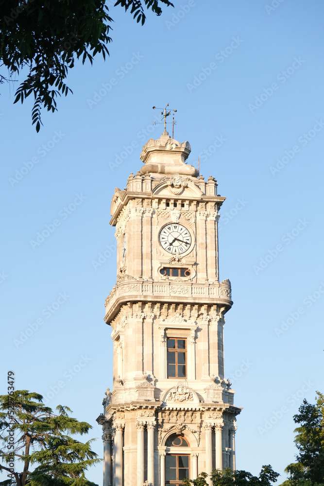 Dolmabahce Clock Tower with trees and blue sky. 