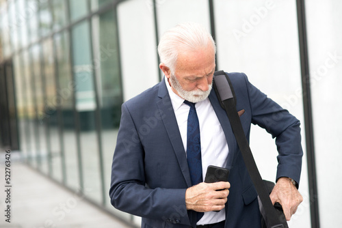 Senior businessman using phone in front of corporate office building