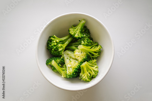 A bowl of cooked green broccoli, shot from above on a light background. Boiled broccoli vegetable in white small bowl for healthy food concept in top view