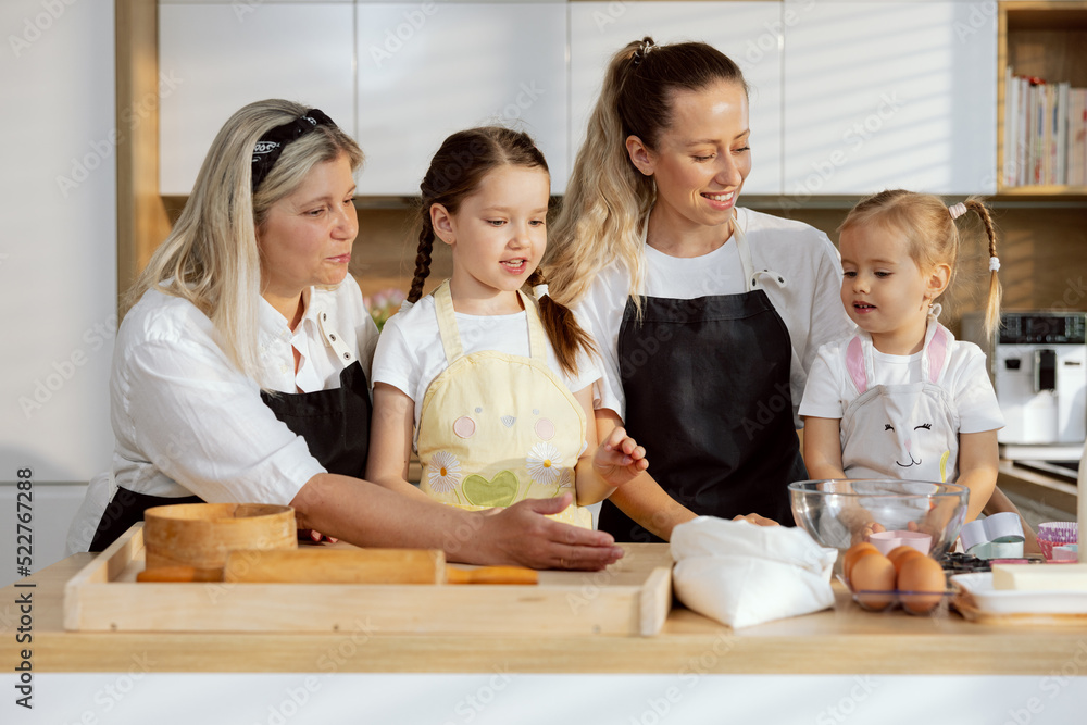 Happy granny daughter and preschooler granchildren cooking baking pie or pizza together in the kitchen . Doing bakery. Women having fun together talking smiling. rolling pin sieve eggs flour. Happy granny daughter and preschooler granchildren cooking baking pie or pizza together in the kitchen . Doing bakery. Women having fun together talking smiling. rolling pin sieve eggs flour.