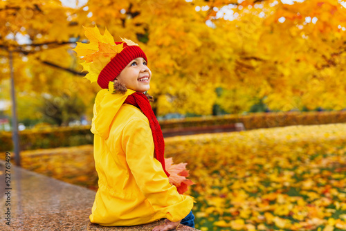 A girl with a wide smile made a crown of red and yellow leaves in an autumn park. Queen of Autumn