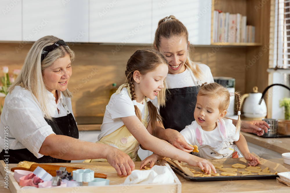 Older daughter and little one putting cookies on baking tray helping mother and granny baking cooking biscuits cookies cakes pie homemade pizza braed. Older daughter and little one putting cookies on baking tray helping mother and granny baking cooking biscuits cookies cakes pie homemade pizza braed.
