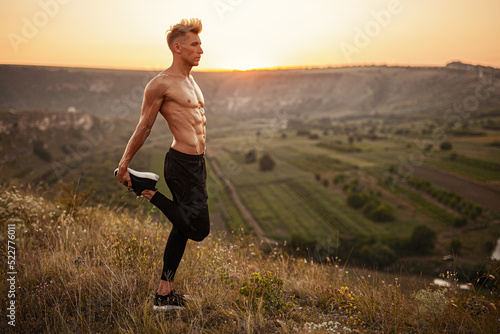 Fit confident sportsman stretching legs on hill slope during outdoor training