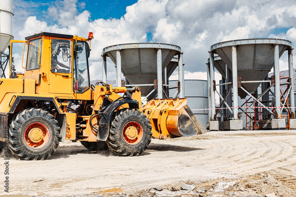 A large front loader transports materials in a concrete production plant. Production of concrete. Transportation of bulk materials. Construction equipment. Bulk cargo transportation.