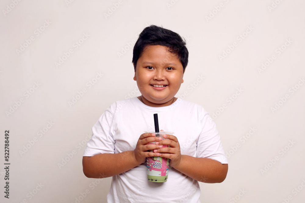 Happy asian boy standing while holding a drinking package. Isolated on white.