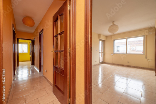 Corridor of a house with reddish wood doors  light stoneware floors and aluminum windows