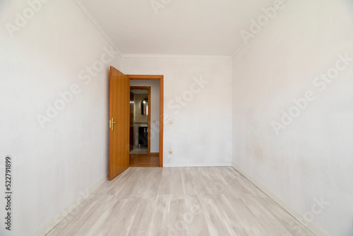 Empty room with white walls  light wood floors and woodwork on the doors