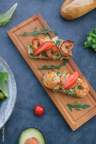 Vediterranean vegetable salad of fresh tomato, olives, capers, onion, spinach, lettuce and sesame on plate. Grillled shrimp bruschetta with salad greens.
