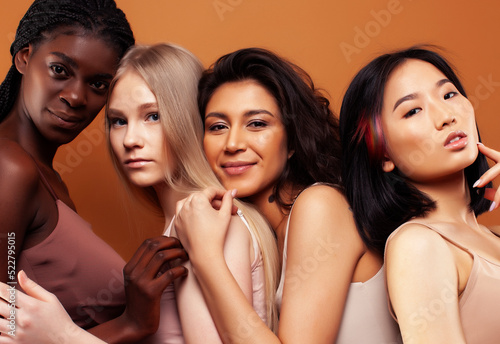 young pretty african and caucasian women posing cheerful together on brown background, lifestyle diverse nationality people concept