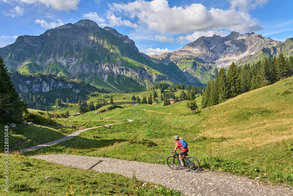 active senior woman, riding her electric mountain bike in the Arlberg mountain range near the famous village of Lech, Tirol, Austrian Alps
