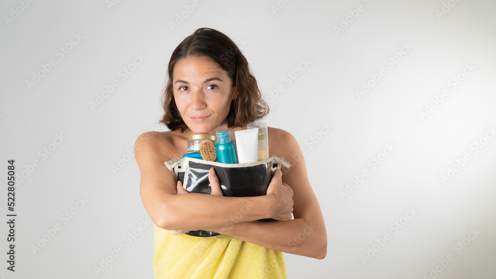 A woman in a towel hugs a cosmetic bag with creams, serum and cosmetics for body and face care A woman in a towel hugs a cosmetic bag with creams, serum and cosmetics for body and face care