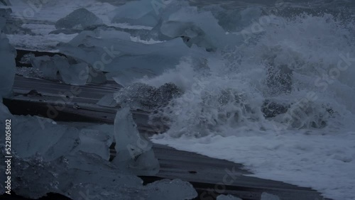 Spectacular waves breaking over ithe black sand beach icebergs in slow-mo photo