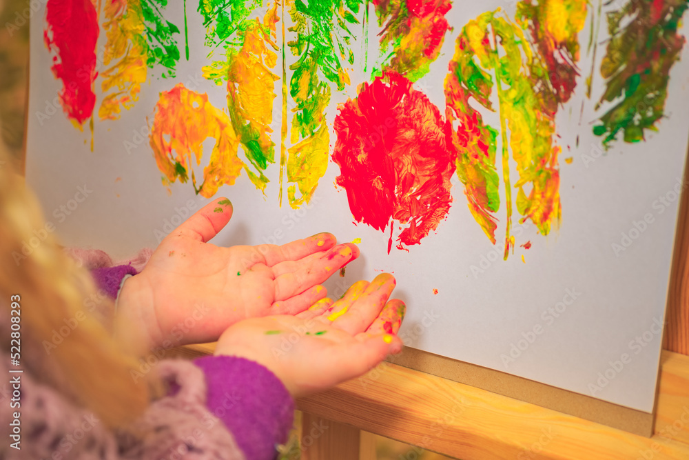 little girl artist with paints in her hands in autumn in the park draws a landscape with leaves on canvas.