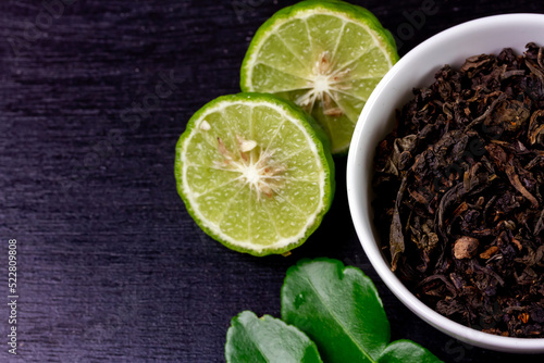 Bergamot tea or Earl Grey tea in white bowl and fresh bergamot fruit on black wooden background.