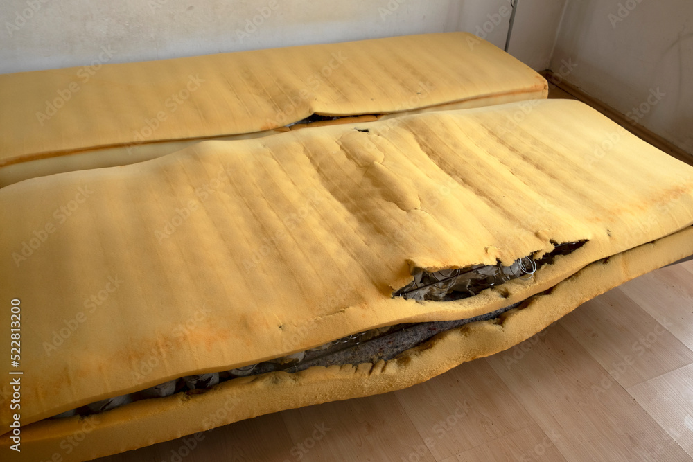 An old tattered foam mattress with protruding springs in a room with