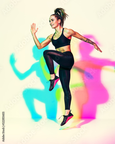 Sporty girl jumping up. Photo of muscular woman in black sportswear on white background with effect of rgb colors shadows. Dynamic movement. Sports motivation and healthy lifestyle