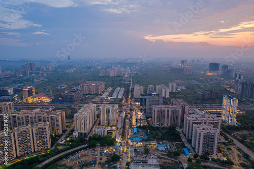 drone aerial shot showing busy traffic filled streets between skyscrapers filled with houses, homes and offices with a red sunset sky showing the hustle and bustle of life in Gurgaon, delhi photo