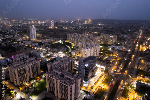 aerial drone shot showing brightly lit orange streets with skyscrapers  towers housing homes offices and shopping complexes in between with the city skyline in the distance in Gurgaon Delhi India