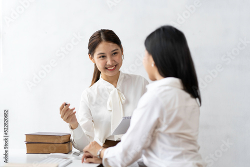 Two beautiful Asian business women who are happy to sit and talk about working together at the office. © crizzystudio