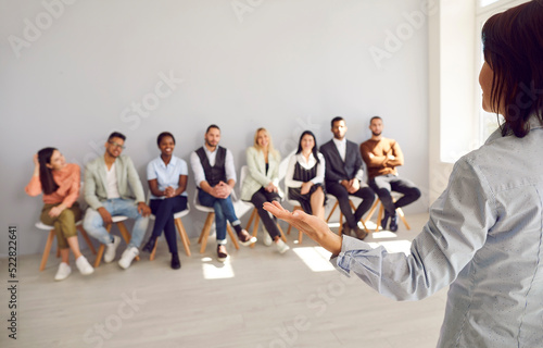 Back view of female speaker talk lead seminar with diverse employees at company training. Woman leader or presenter make speech head briefing with colleagues in office. Leadership concept.