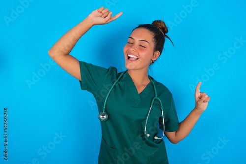 Fototapeta Naklejka Na Ścianę i Meble -  Photo of upbeat beautiful doctor woman wearing medical uniform over blue background has fun and dances carefree wear being in perfect mood makes movements. Spends free time on disco party