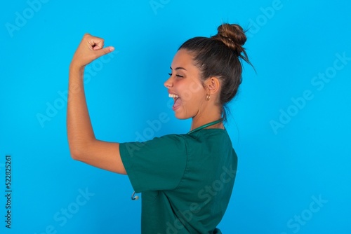 Profile photo of beautiful doctor woman wearing medical uniform over blue background supporting soccer team World Cup 2022 raise fist shouting