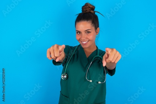 beautiful doctor woman wearing medical uniform over blue background cheerful and smiling poiting at camera