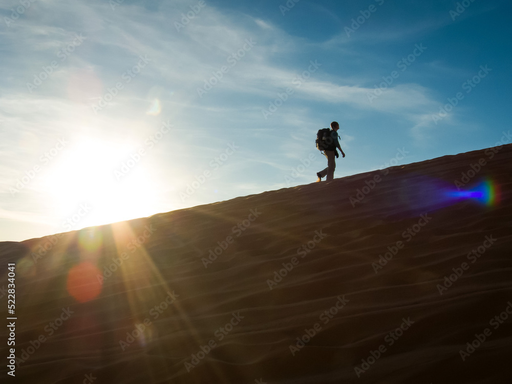 Adventurer climbs a sand dune against the backdrop of the setting sun Adventurer climbs a sand dune against the backdrop of the setting sun