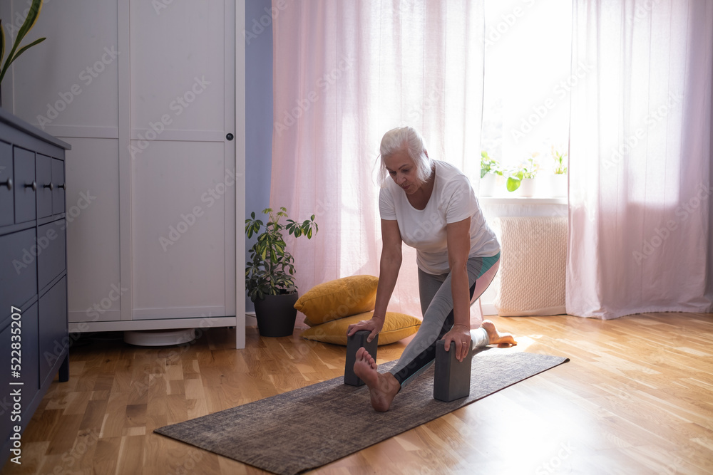 Senior aged woman sitting on the yoga mat and stretching her legs