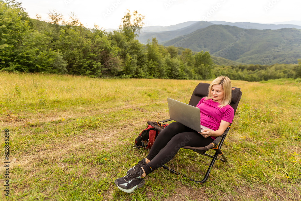 A woman in a sports warm suit works on a laptop outdoors in a mountainous area. A woman in a sports warm suit works on a laptop outdoors in a mountainous area.