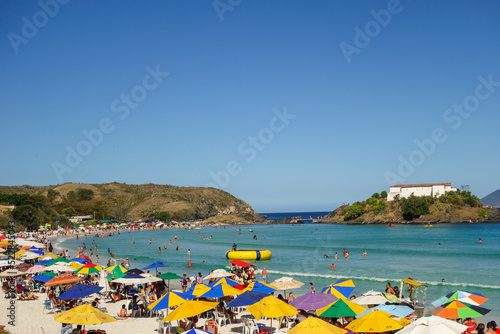 colorful umbrellas and tourists crowd the sand line at Praia do Forte in Cabo Frio, Rio de Janeiro, Brazil © Caio
