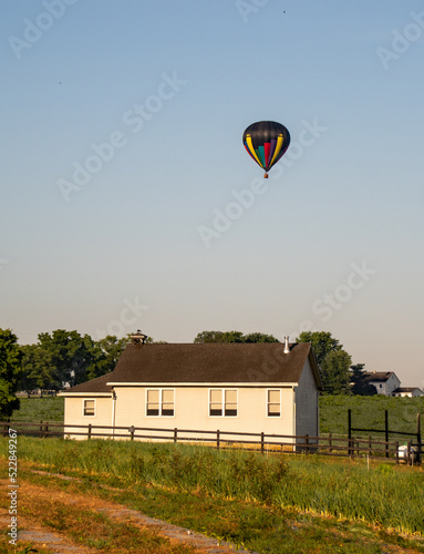 Hot air balloons rise in the sky behind an Amish school in the early morning hours of on a summer day. 