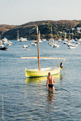 Adulto tomando un baño junto a los barcos al atardecer frente a la costa de Cadaqués en la Costa Brava, Cataluña.