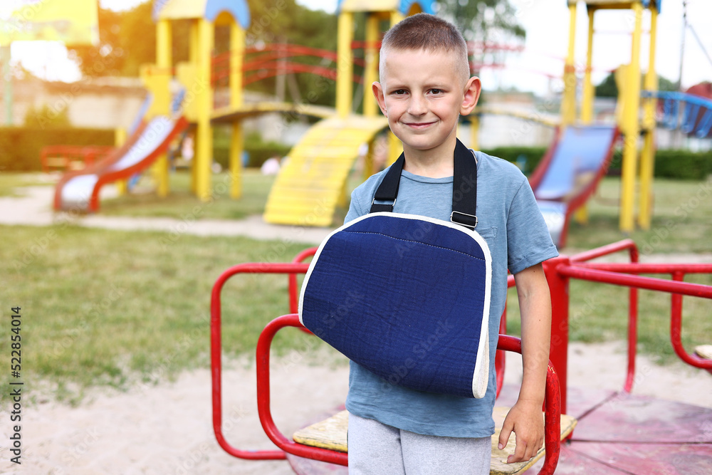 happy child with broken limb arm outdoors on playground background. school boy had accident on summer vacation. kid in a cast on hand. concept of health and medical. happy child with broken limb arm outdoors on playground background. school boy had accident on summer vacation. kid in a cast on hand. concept of health and medical.