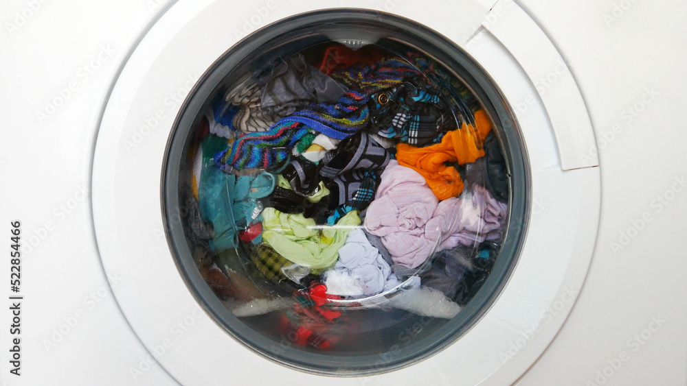 Close-up of the drum of a washing machine with various colored clothes inside of it Close-up of the drum of a washing machine with various colored clothes inside of it