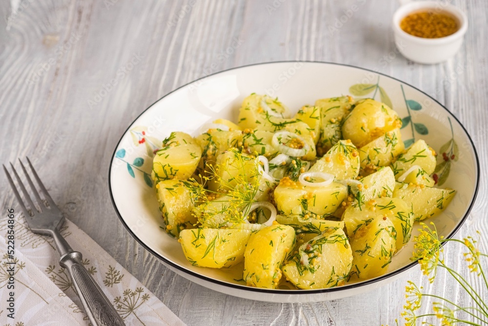 A simple boiled potato salad with onions, dill and mustard dressing in a white bowl on a light wooden background. Scandinavian style, food. A simple boiled potato salad with onions, dill and mustard dressing in a white bowl on a light wooden background. Scandinavian style, food.