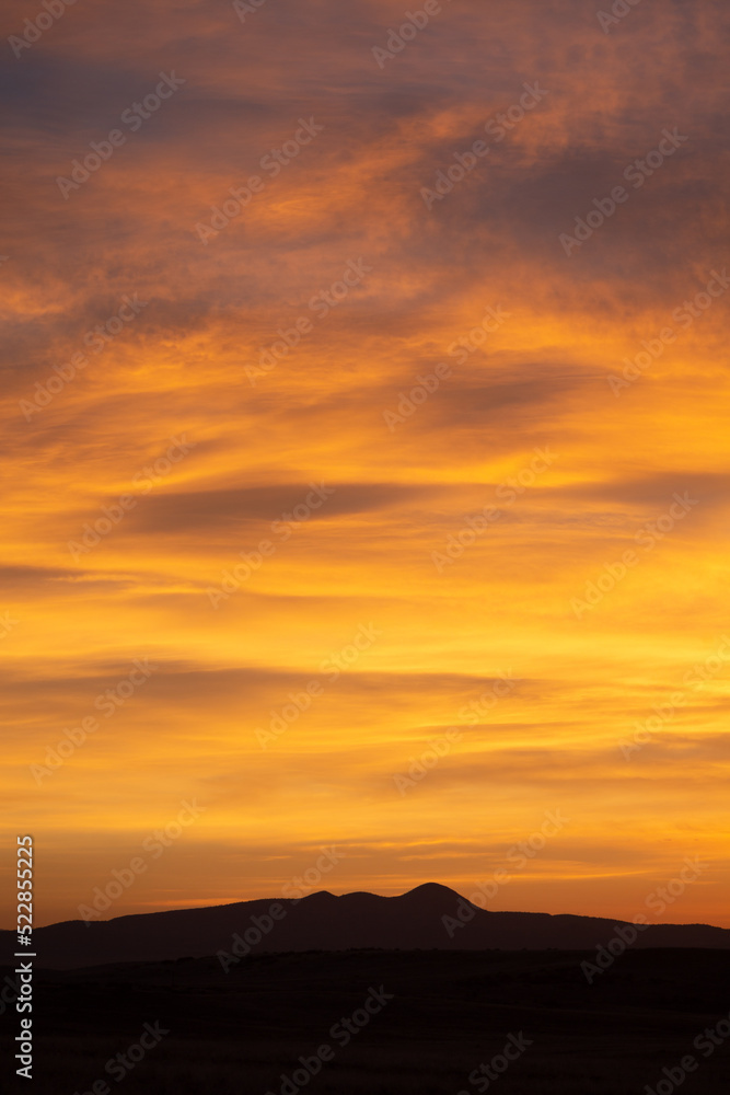 Obraz premium Vivid yellow sunrise over silhouette mountain peak range vertical