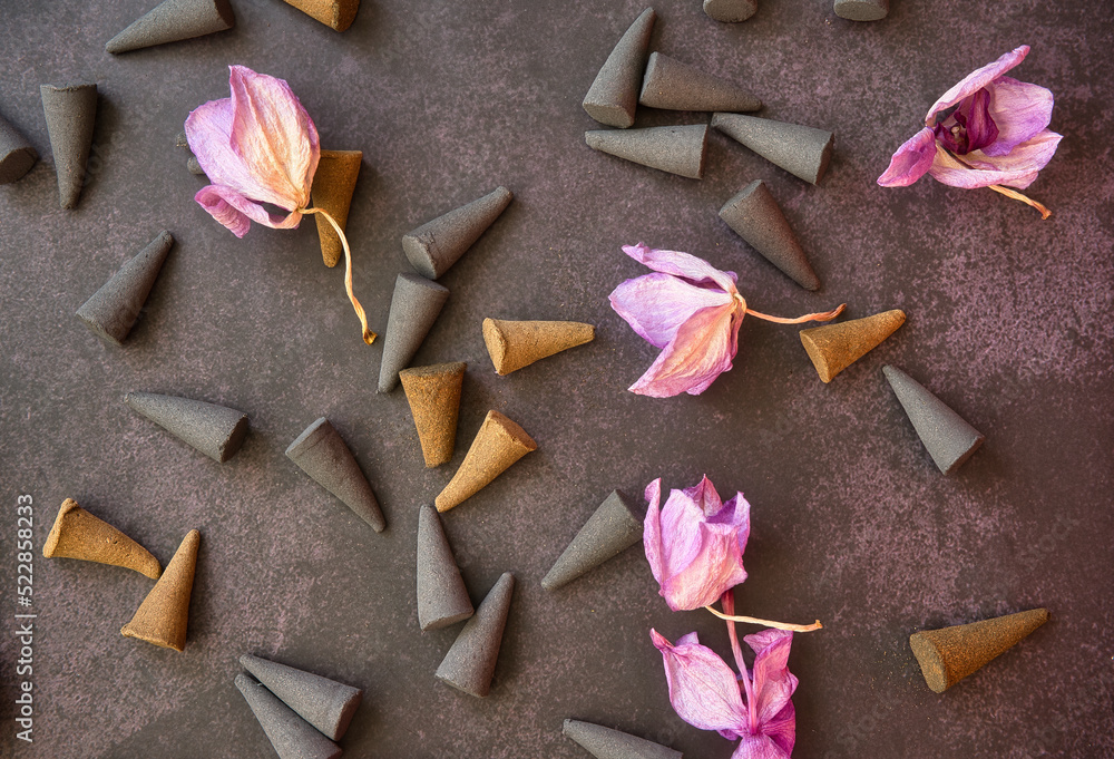 Variety of cone-shaped incense sticks and dried violet flowers on a dark background. Variety of cone-shaped incense sticks and dried violet flowers on a dark background.