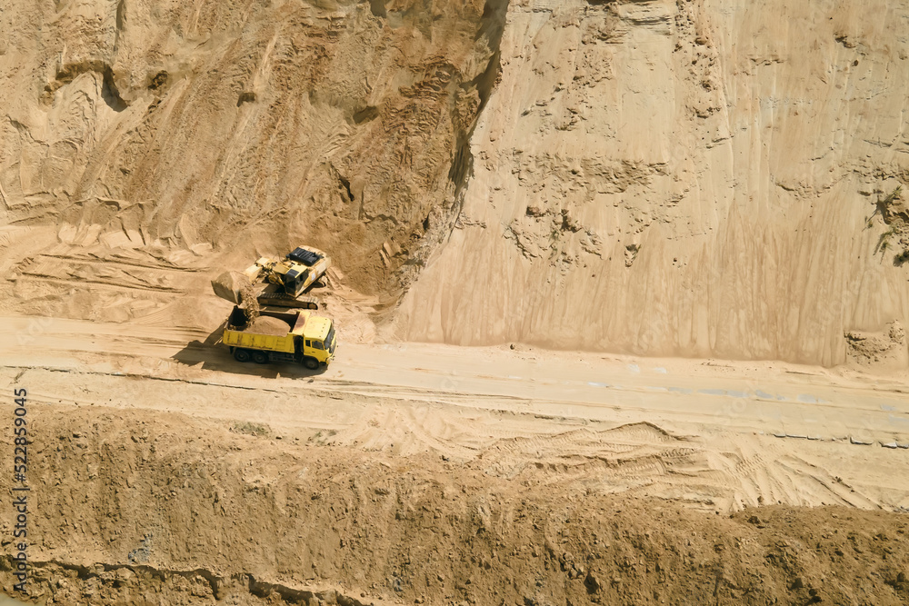Aerial view of excavator loading sand into empty dump truck in open air sand ballast quarry Aerial view of excavator loading sand into empty dump truck in open air sand ballast quarry