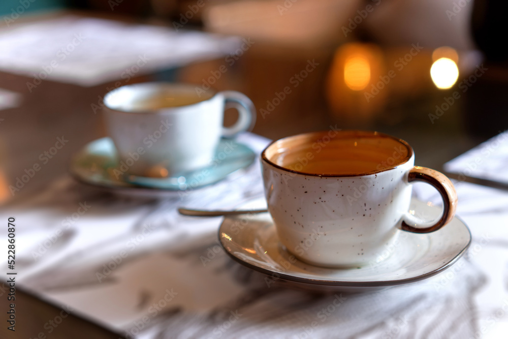 Orange and blue cups on saucers. The mugs with tea in soft focus standing on menu papers on naturally blurred background. Coffee, tea house, bokeh lights. The concept of a cozy pastime