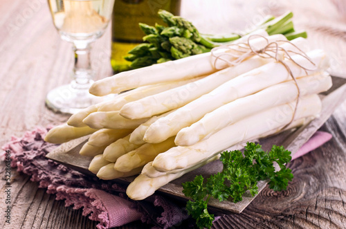 Fresh raw green and white asparagus bundle offered as close-up on wooden shabby chic tray