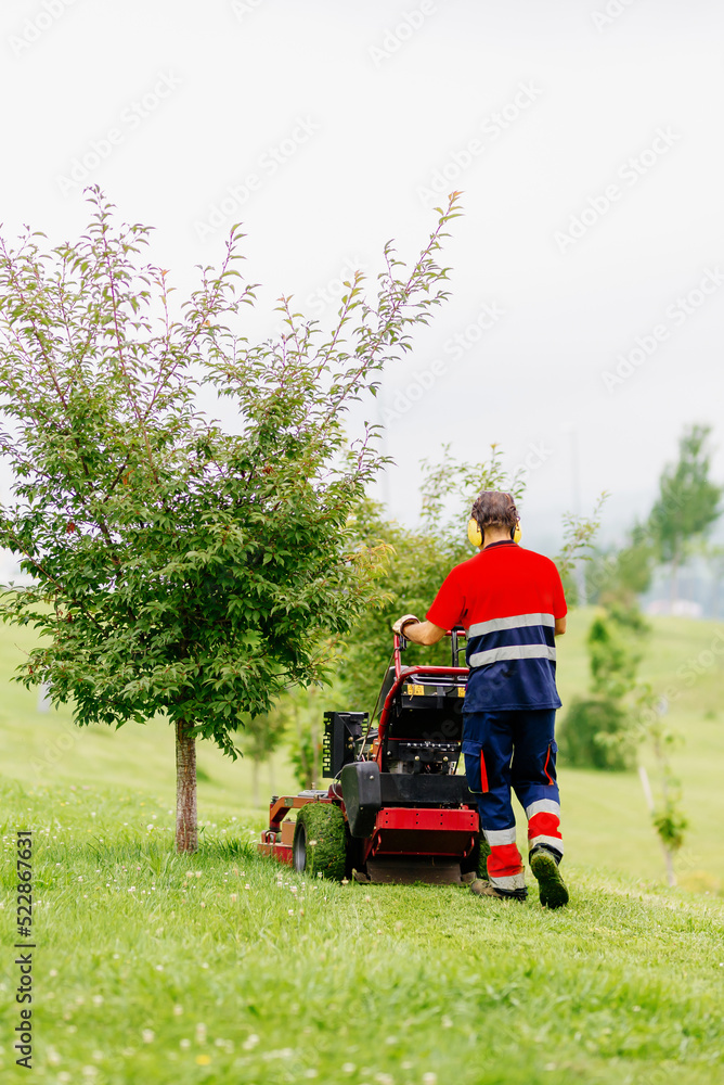 gardening officer in uniform working with a lawn mower. Unrecognizable man mowing a field.