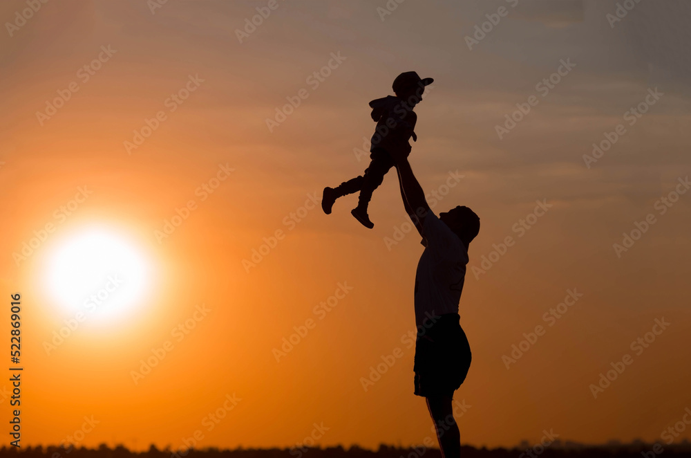 Father and son play in the park during sunset. People have fun in nature. Dark silhouettes of people on an orange background.The concept of a friendly family and summer holidays and Father's Day. Father and son play in the park during sunset. People have fun in nature. Dark silhouettes of people on an orange background.The concept of a friendly family and summer holidays and Father's Day.