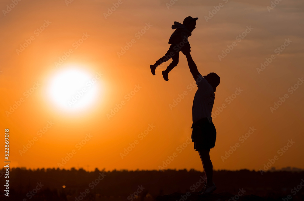 Father and son play in the park during sunset. People have fun in nature. Dark silhouettes of people on an orange background.The concept of a friendly family and summer holidays and Father's Day.
