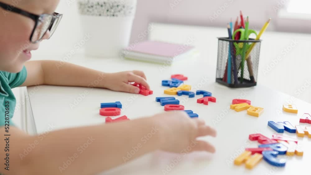 smart baby boy in eyeglasses sitting at table putting abc letters in word toy, child learning to complete words, learning alphabet. early kids education at home. 4 year boy playing with colorful toys smart baby boy in eyeglasses sitting at table putting abc letters in word toy, child learning to complete words, learning alphabet. early kids education at home. 4 year boy playing with colorful toys